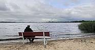 Ein Mann sitzt auf einer Bank am Ufer eines Sees.